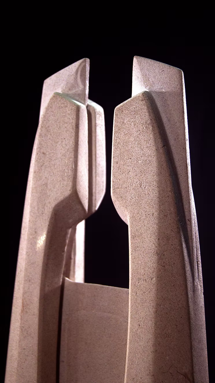 Stone sculpture featuring two tall, curved spires carved from Purbeck Thornback stone, set on a polished black granite base, connected by a narrow central opening with stainless steel elements, displayed against a dark background.