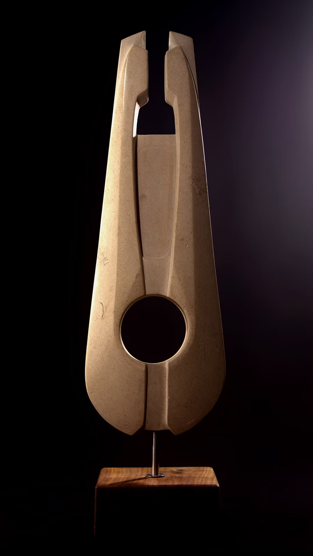 Stone sculpture featuring two tall, curved spires carved from Purbeck Thornback stone, set on a polished black granite base, connected by a narrow central opening with stainless steel elements, displayed against a dark background.