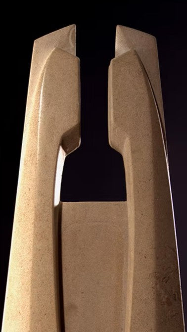 Stone sculpture featuring two tall, curved spires carved from Purbeck Thornback stone, set on a polished black granite base, connected by a narrow central opening with stainless steel elements, displayed against a dark background.