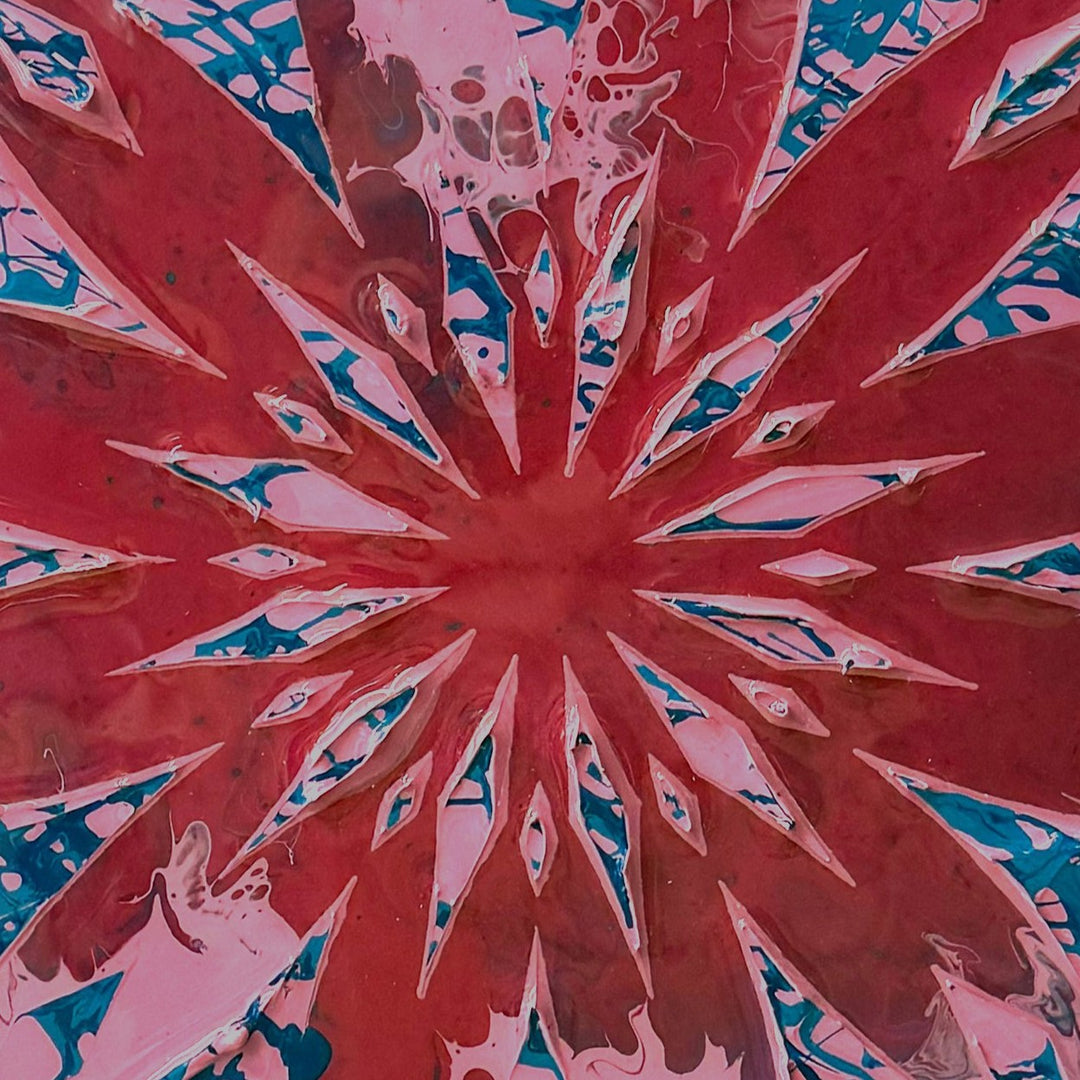Circular contemporary wall artwork by Mike Philp featuring radiating geometric forms cutting through fluid fields of red, pink and blue. Sharp structure contrasts with organic movement beneath a high-gloss resin surface, creating depth, energy, and controlled expansion.