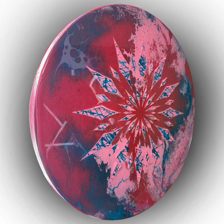 Circular contemporary wall artwork by Mike Philp featuring radiating geometric forms cutting through fluid fields of red, pink and blue. Sharp structure contrasts with organic movement beneath a high-gloss resin surface, creating depth, energy, and controlled expansion.