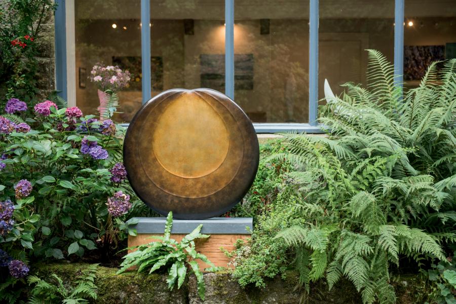 Circular bronze sculpture by Dominic Welch, Aurorean Moon, featuring a layered, concentric form with a glowing turquoise-green patina at its centre, radiating outwards into rich bronze and earthy red-gold tones. A refined limited-edition work blending celestial inspiration with organic presence.