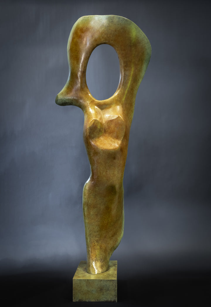 Abstract bronze sculpture of a stylised female torso with flowing curves and a hollowed circular form near the head, displayed in various outdoor and indoor settings. The sculpture has a rich patinated surface with green, gold, and bronze tones.
