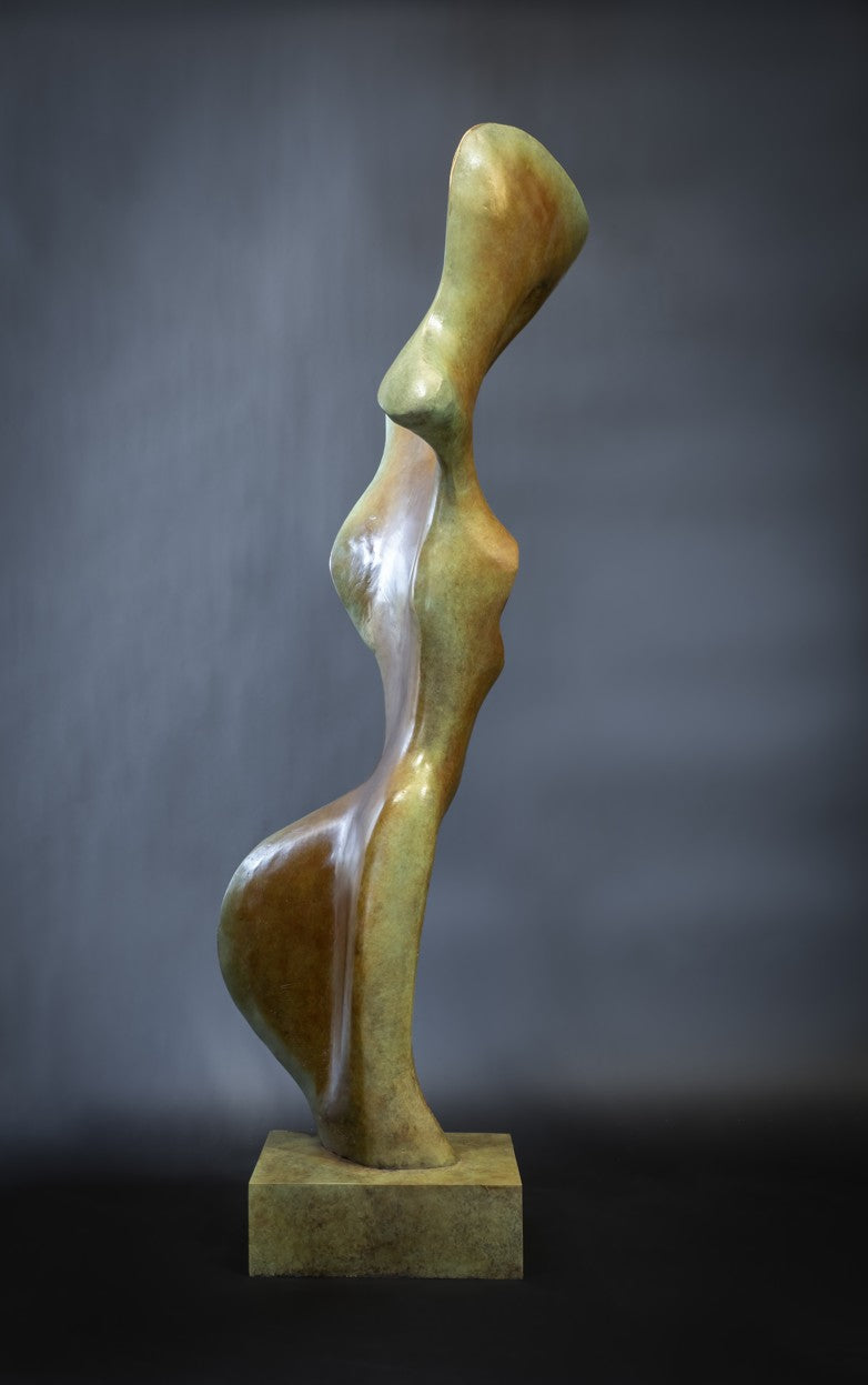 Abstract bronze sculpture of a stylised female torso with flowing curves and a hollowed circular form near the head, displayed in various outdoor and indoor settings. The sculpture has a rich patinated surface with green, gold, and bronze tones.