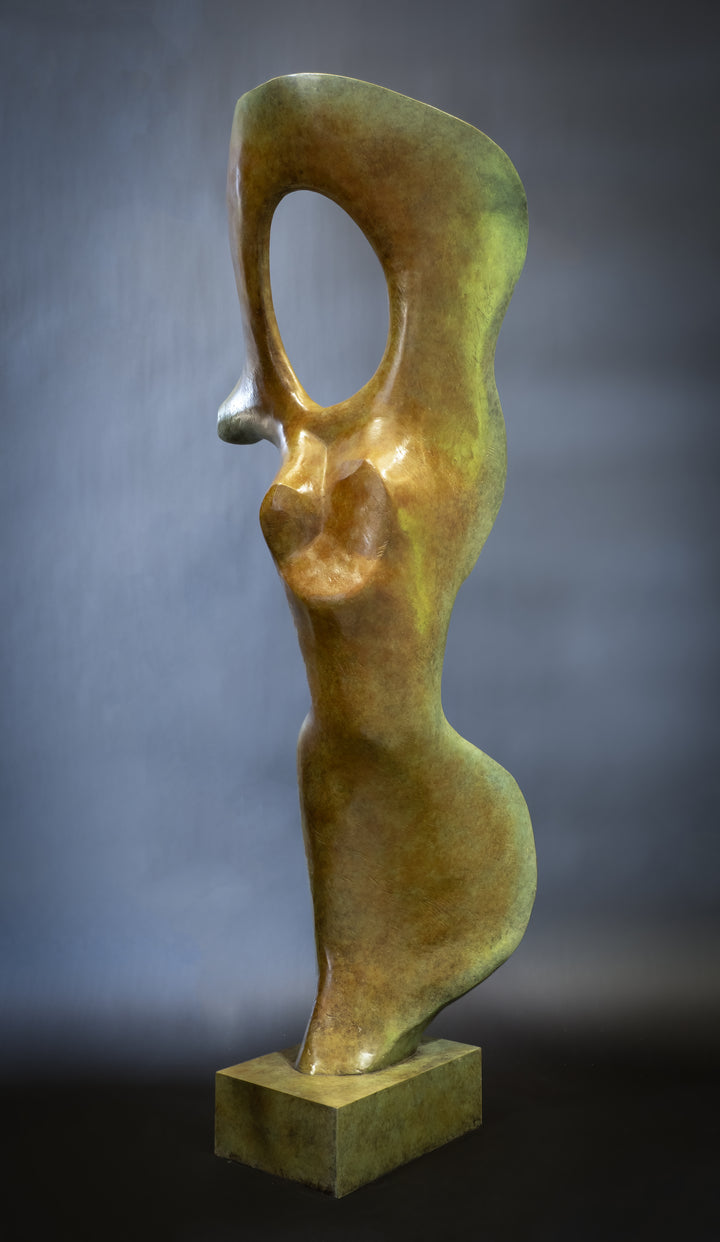Abstract bronze sculpture of a stylised female torso with flowing curves and a hollowed circular form near the head, displayed in various outdoor and indoor settings. The sculpture has a rich patinated surface with green, gold, and bronze tones.