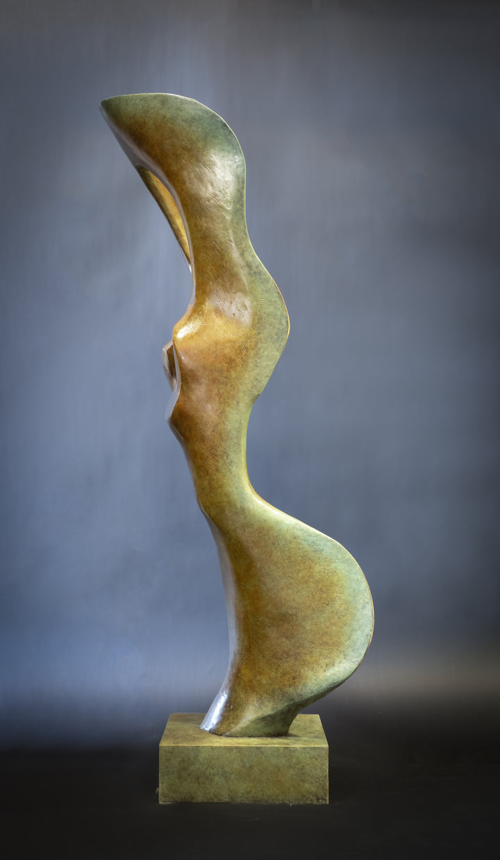 Abstract bronze sculpture of a stylised female torso with flowing curves and a hollowed circular form near the head, displayed in various outdoor and indoor settings. The sculpture has a rich patinated surface with green, gold, and bronze tones.