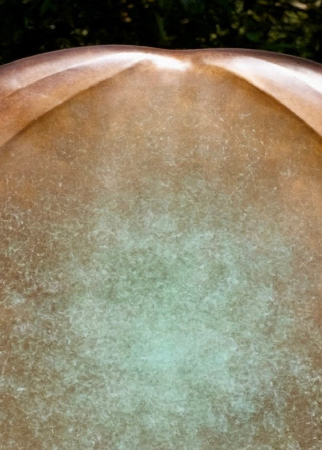 Large circular bronze sculpture Aegean Moon by Dominic Welch, with a luminous verdigris centre fading into warm bronze tones. The surface has subtle textural rings, evoking the phases of the moon. Displayed outdoors among woodland and seasonal landscapes, the piece radiates presence and calm.