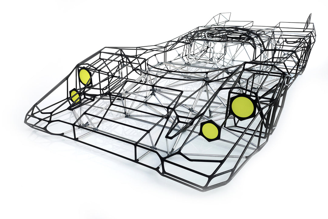Large skeletal sculpture of a Porsche 917 race car, half-size, created from black carbon fibre and aluminium rods with yellow headlight details — an intricate polygonal framework inspired by the 1971 Le Mans–winning Porsche 917K.