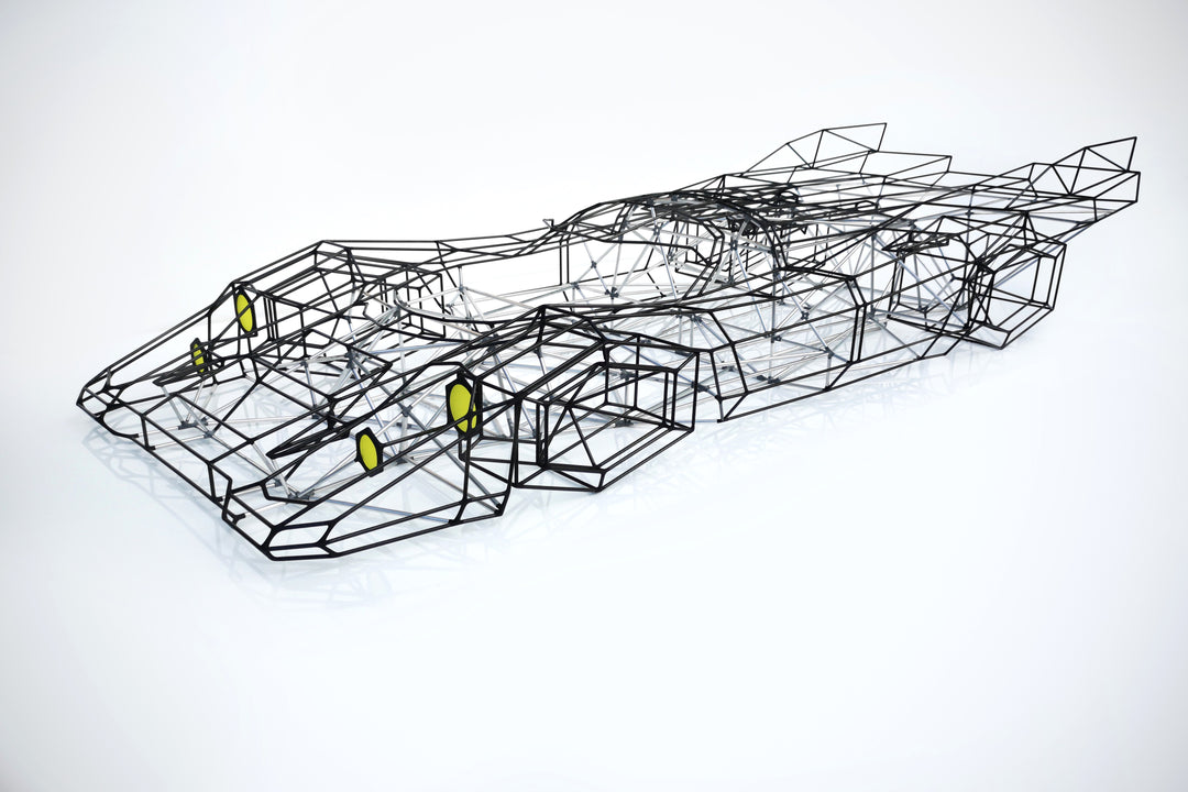 Large skeletal sculpture of a Porsche 917 race car, half-size, created from black carbon fibre and aluminium rods with yellow headlight details — an intricate polygonal framework inspired by the 1971 Le Mans–winning Porsche 917K.