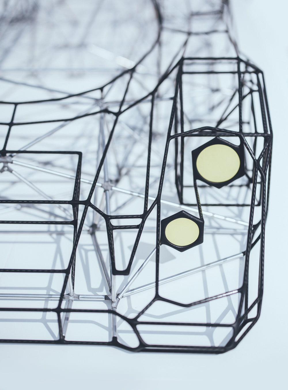 Large skeletal sculpture of a Porsche 917 race car, half-size, created from black carbon fibre and aluminium rods with yellow headlight details — an intricate polygonal framework inspired by the 1971 Le Mans–winning Porsche 917K.