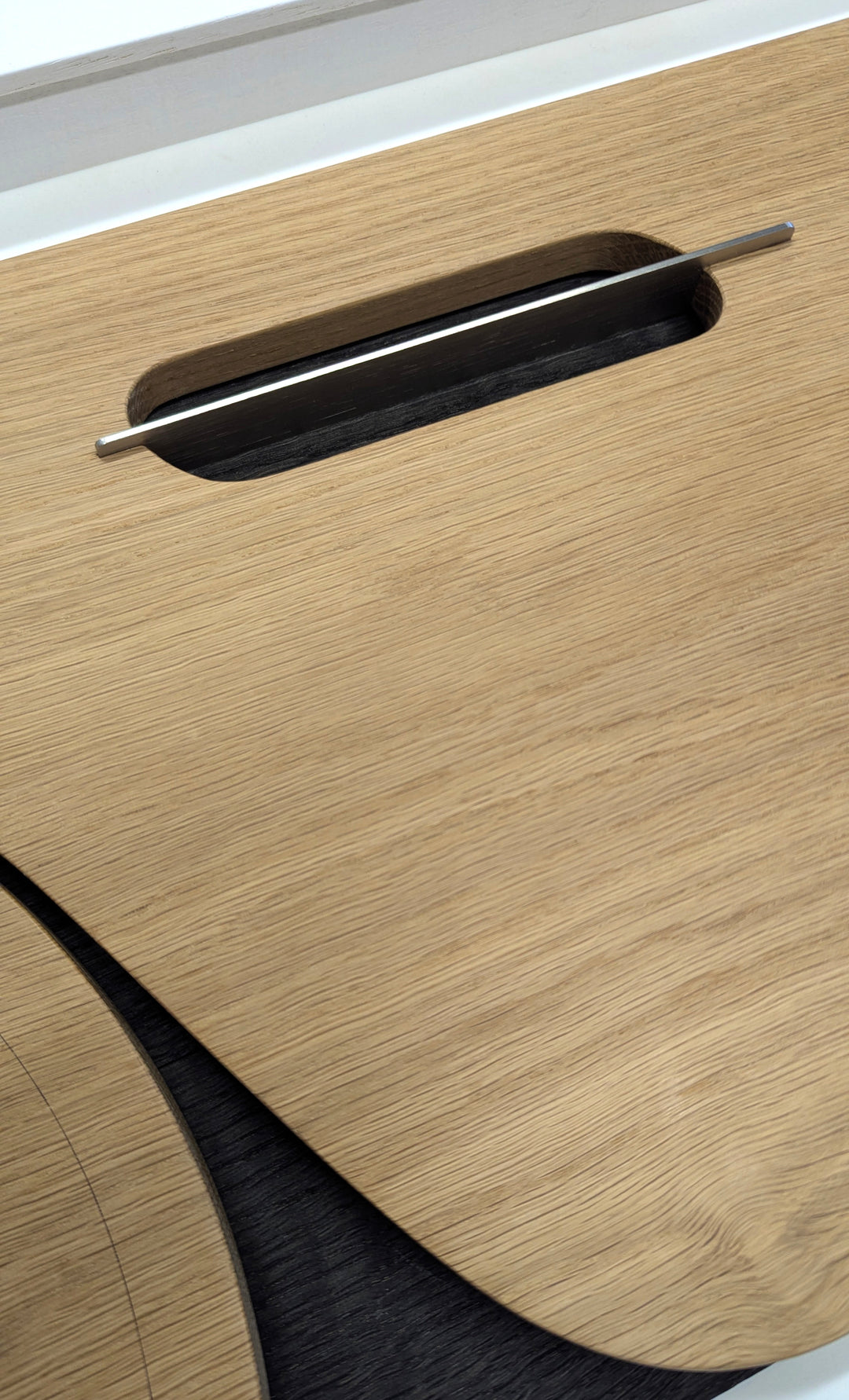 Jonny Ambrose minimalist oak wall sculpture featuring the side profile of an Aston Martin DB5 with carved wheel arch and signature side vent, accented with aluminium detail on a white Corian backdrop.