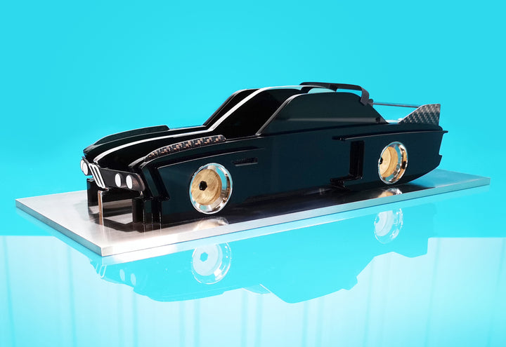 Sculptural model of the 1970s BMW E9 “Batmobile” touring car by Jonny Ambrose — a black, layered acrylic and carbon fibre form with polished aluminium details on a brushed acrylic plinth, capturing its dramatic wings and flared racing silhouette.