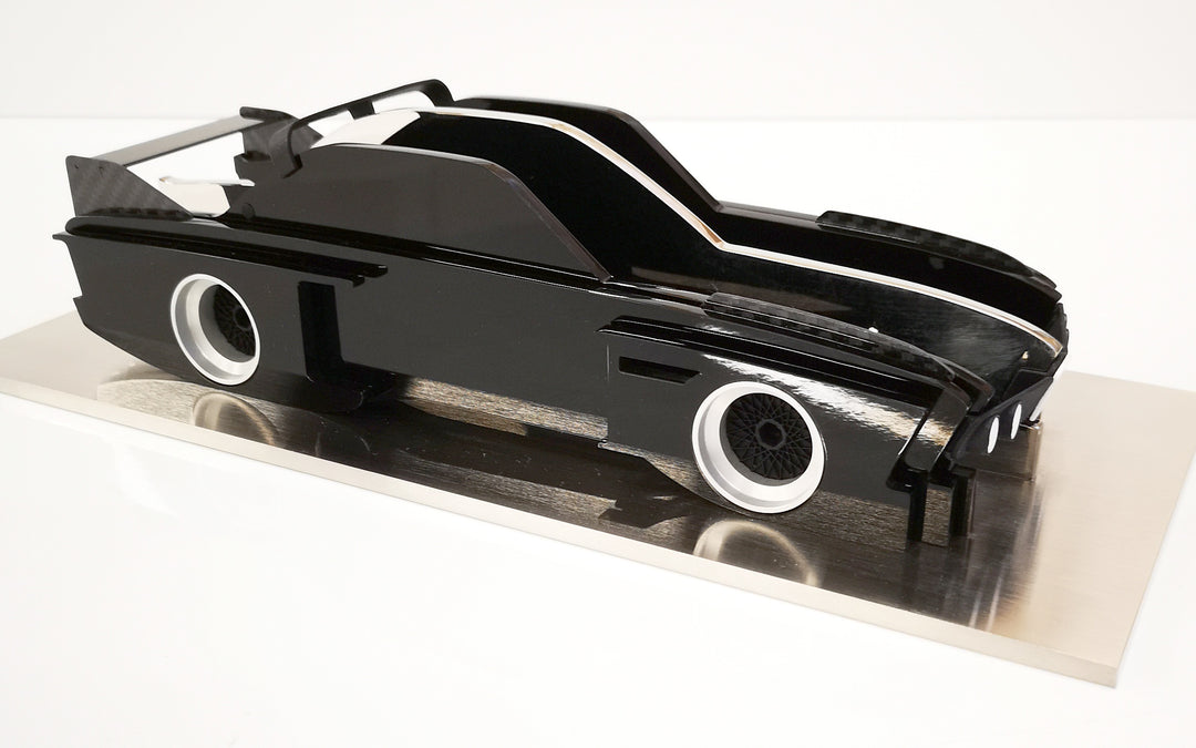 Sculptural model of the 1970s BMW E9 “Batmobile” touring car by Jonny Ambrose — a black, layered acrylic and carbon fibre form with polished aluminium details on a brushed acrylic plinth, capturing its dramatic wings and flared racing silhouette.