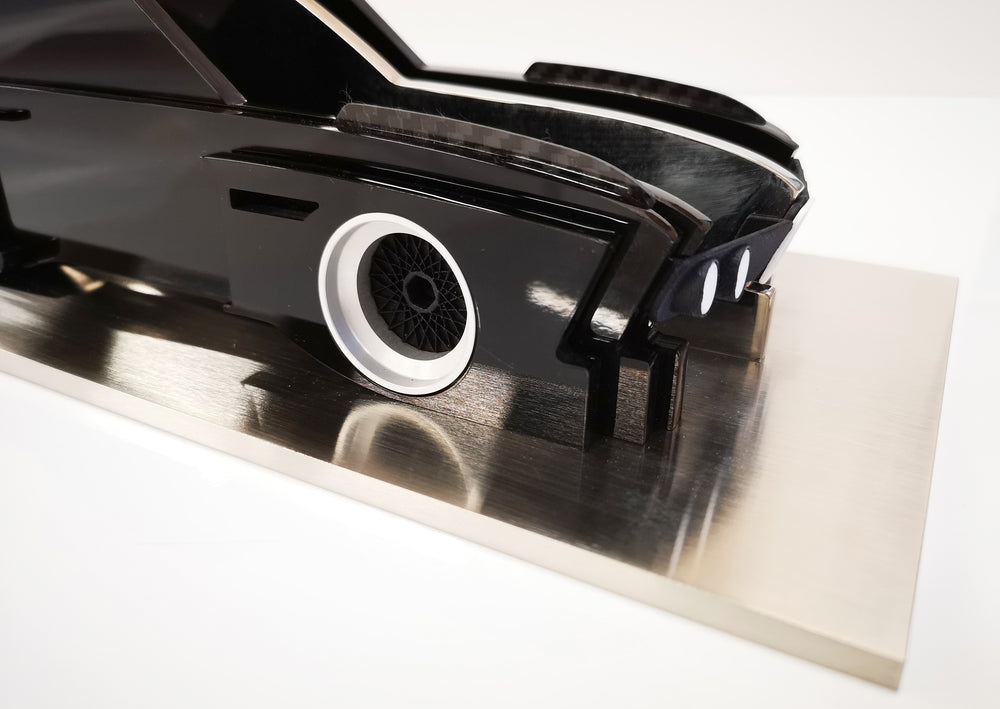 Sculptural model of the 1970s BMW E9 “Batmobile” touring car by Jonny Ambrose — a black, layered acrylic and carbon fibre form with polished aluminium details on a brushed acrylic plinth, capturing its dramatic wings and flared racing silhouette.