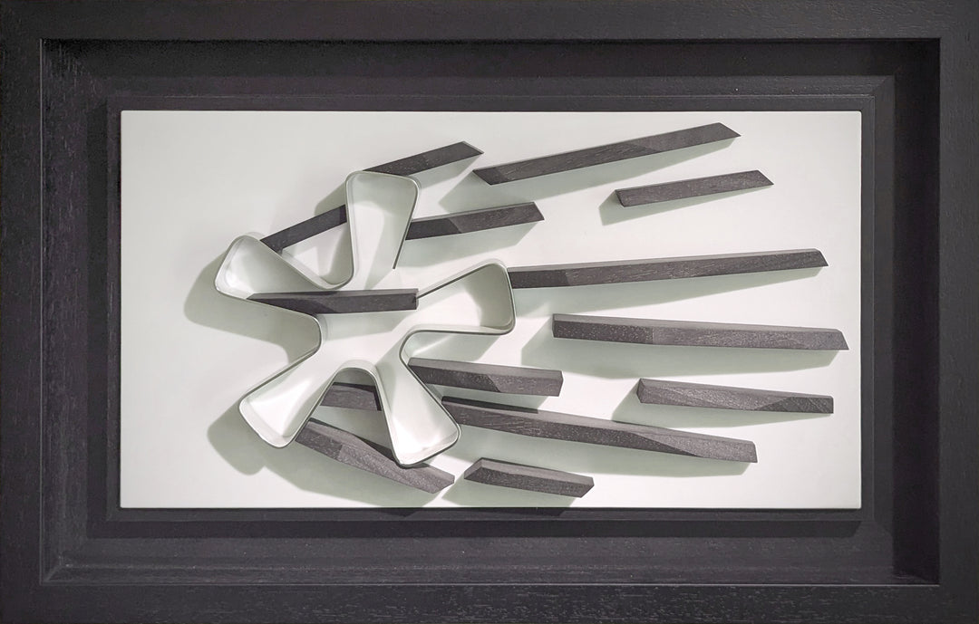 Abstract automotive wall sculpture by Jonny Ambrose featuring a polished aluminium Fuchs wheel with black wooden shards radiating outward to suggest power-slide motion and speed, set on a clean white Corian background with black frame.