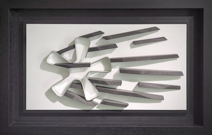 Abstract automotive wall sculpture by Jonny Ambrose featuring a polished aluminium Fuchs wheel with black wooden shards radiating outward to suggest power-slide motion and speed, set on a clean white Corian background with black frame.