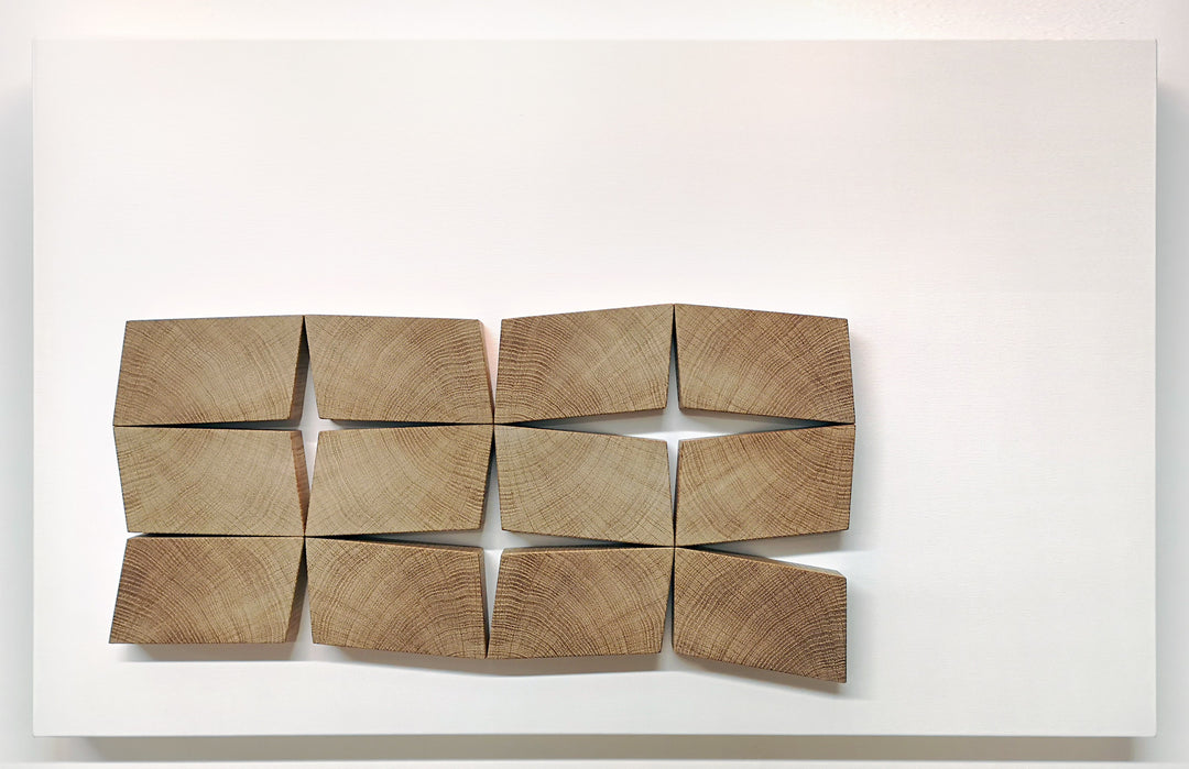 Abstract oak wall sculpture by Jonny Ambrose — twelve angled endgrain oak blocks arranged to shift and expand across a clean white canvas, creating depth, movement, and warm natural texture.