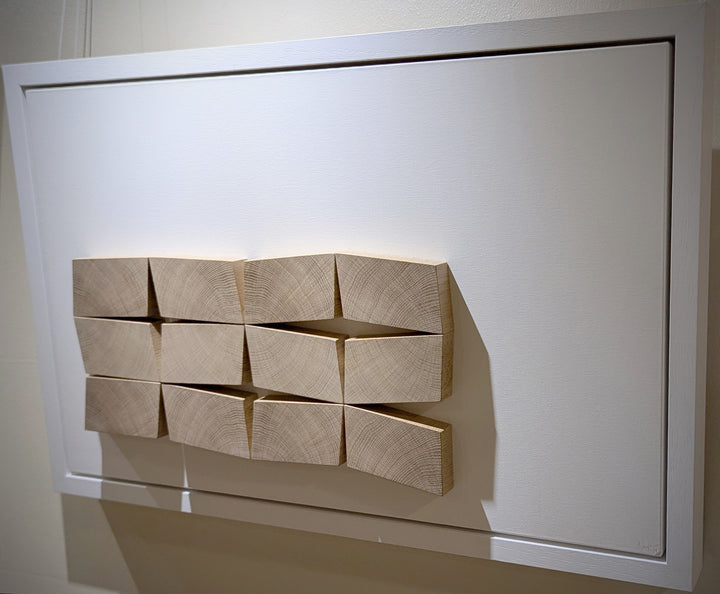 Abstract oak wall sculpture by Jonny Ambrose — twelve angled endgrain oak blocks arranged to shift and expand across a clean white canvas, creating depth, movement, and warm natural texture.