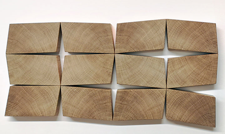 Abstract oak wall sculpture by Jonny Ambrose — twelve angled endgrain oak blocks arranged to shift and expand across a clean white canvas, creating depth, movement, and warm natural texture.