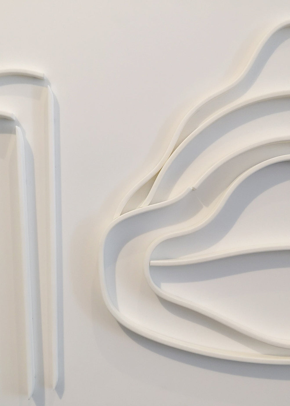 Minimalist white wall sculpture of a 1930s Mercedes W154 Grand Prix car by Jonny Ambrose — abstract flowing lines in thermoformed Corian creating an elegant automotive relief with deep black frame.