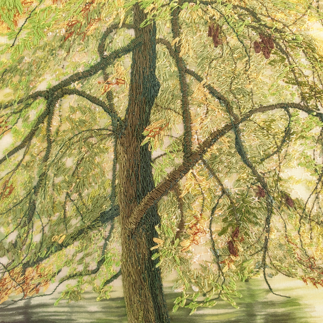 Embroidered woodland scene with moss-covered tree trunks, autumn leaves on the forest floor, and a calm river reflecting soft light.