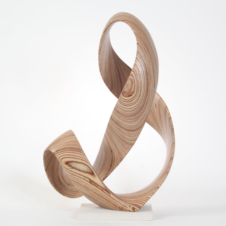 Hand-carved birch plywood sculpture by Bill Prickett, formed as a flowing Möbius-style infinity loop inspired by an ampersand, with continuous twisting curves, visible layered grain, and a balanced sculptural presence on a white base.