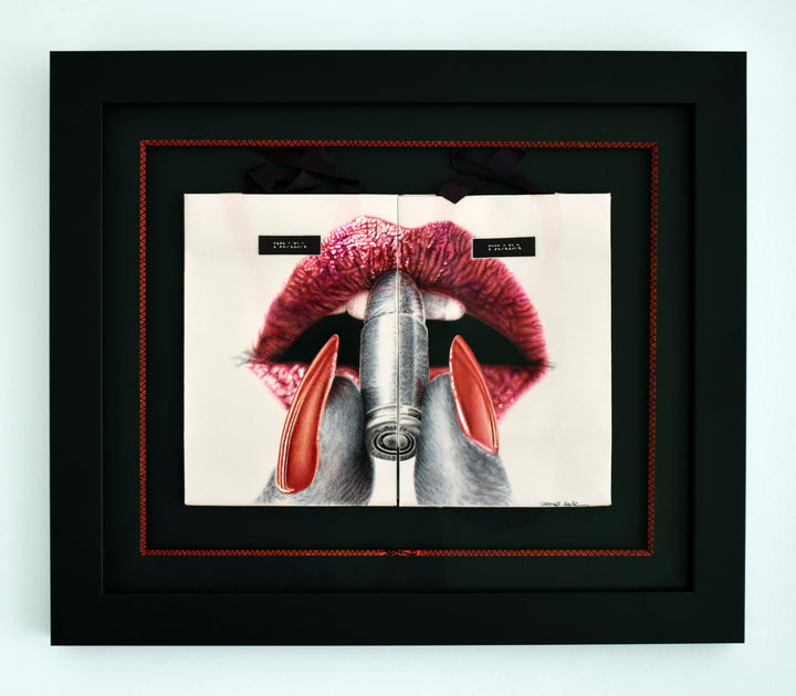 Original artwork titled “Apply With Caution” by James Mylne, featuring a provocative hyperrealistic drawing of glossy red lips applying lipstick formed from a bullet. Created using red and black ballpoint pens and acrylic marker on two Prada gift bags, the work is framed in a black box frame with red detailing and ribbon handles exposed.