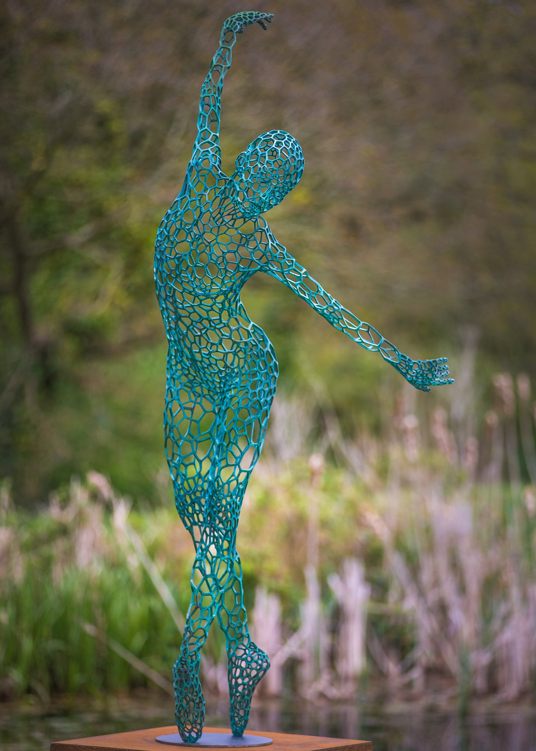 Simon Gudgeon bronze sculpture Athena featuring an elegant open lattice female form with blue green patina displayed within a landscaped outdoor garden setting.