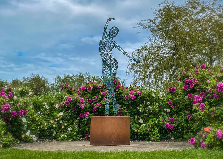 Simon Gudgeon bronze sculpture Athena featuring an elegant open lattice female form with blue green patina displayed within a landscaped outdoor garden setting.