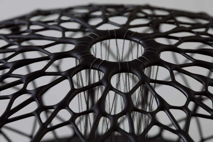 Aulisca Series 2 by Tracy Nicholls — a unique kiln-formed glass sculpture with thread and wood. The piece features two symmetrical domed halves of black glass latticework, fused and slumped into a precise geometric form. Delicate strands of thread stitch the halves together at twenty points, creating a central column that adds both visual tension and structural detail. The sandblasted matte surface contrasts with the subtle inner sheen, casting intricate shadows that shift with the light