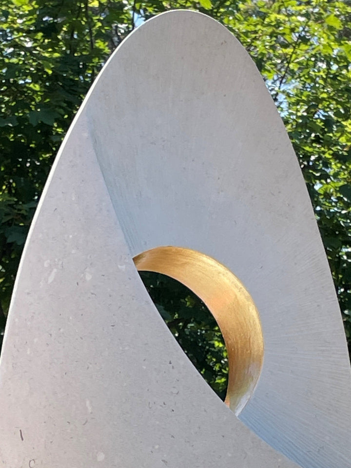 Auric Dawn by Nicola Axe — smooth teardrop-shaped Portland stone sculpture with a precision-cut circular void lined in shimmering gold leaf, set on a mixed oak and granite plinth, minimal yet meditative in form.