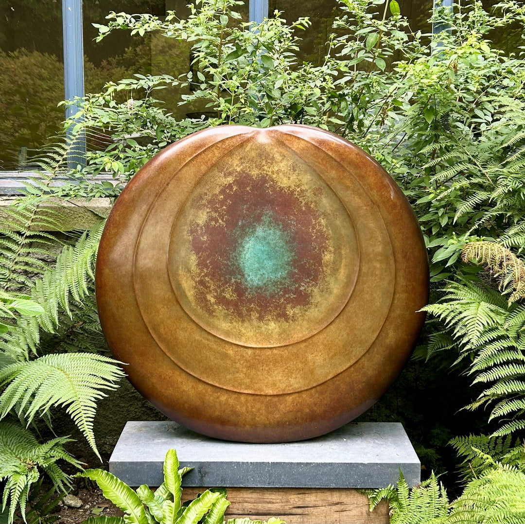 Circular bronze sculpture by Dominic Welch, Aurorean Moon, featuring a layered, concentric form with a glowing turquoise-green patina at its centre, radiating outwards into rich bronze and earthy red-gold tones. A refined limited-edition work blending celestial inspiration with organic presence.