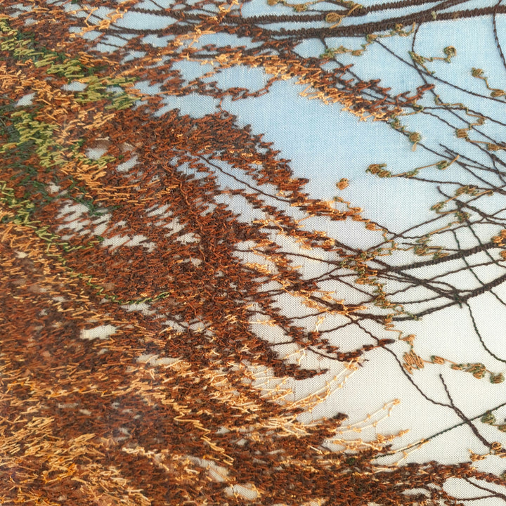 Tall embroidered artwork of a quiet road lined with autumnal trees in golden brown and orange thread, under a pale blue sky.