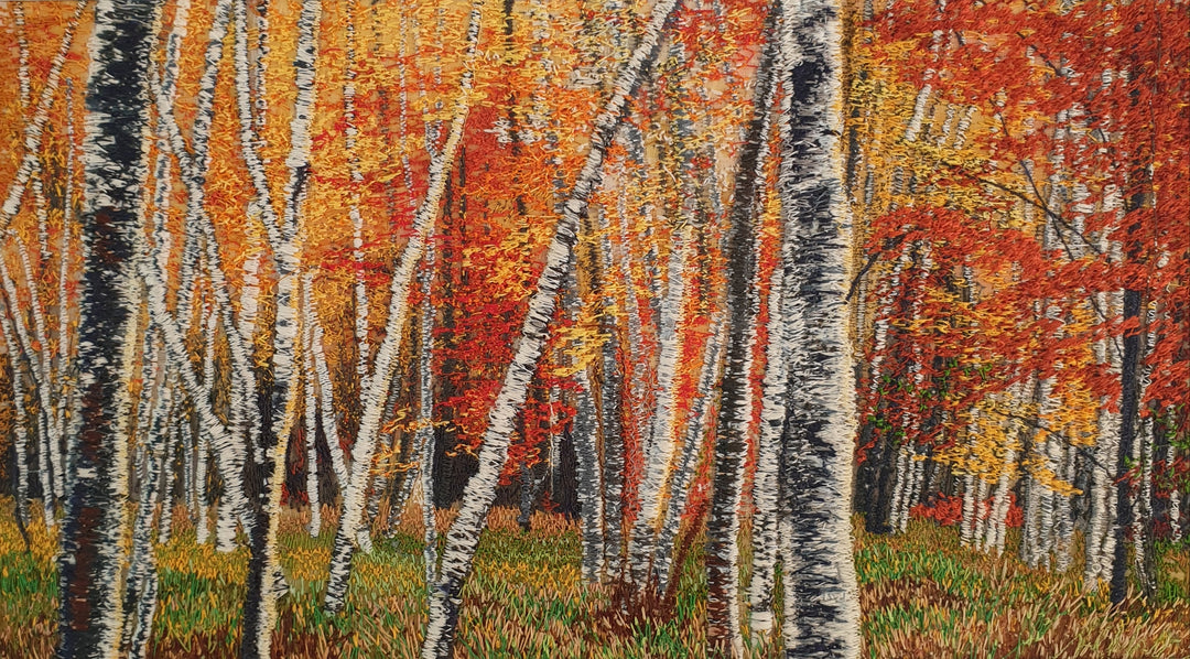 Dense embroidered birch forest in full autumn colour with fiery red, orange, and golden yellow foliage above a grassy woodland floor.