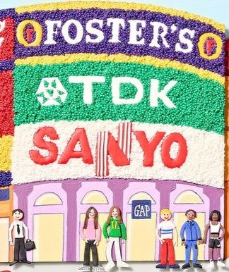 A vibrant, three-dimensional polymer clay artwork of Piccadilly Circus, featuring the iconic curved billboard with brands like Coca-Cola, McDonald’s, and TDK rendered in colourful textured beads. The street scene below includes a classic red double-decker bus marked “38 Piccadilly Circus,” a London black cab, and crowds of joyful figures in bright handmade outfits. Sculpted pigeons dot the grey stone steps beneath the Shaftesbury Memorial Fountain with a golden winged Eros above. 