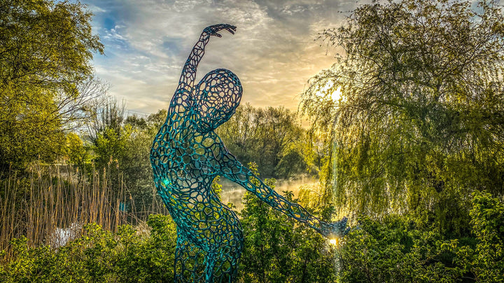 Simon Gudgeon bronze sculpture Athena featuring an elegant open lattice female form with blue green patina displayed within a landscaped outdoor garden setting.