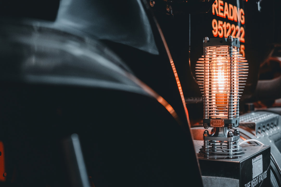 Industrial-style PNEU LAMP handcrafted from disused pneumatic cylinders, featuring layered aluminium and copper fins with a central exposed filament bulb. Designed by Bear Industries as a sculptural lighting piece with a nod to vintage ‘Tilly’ lamps.