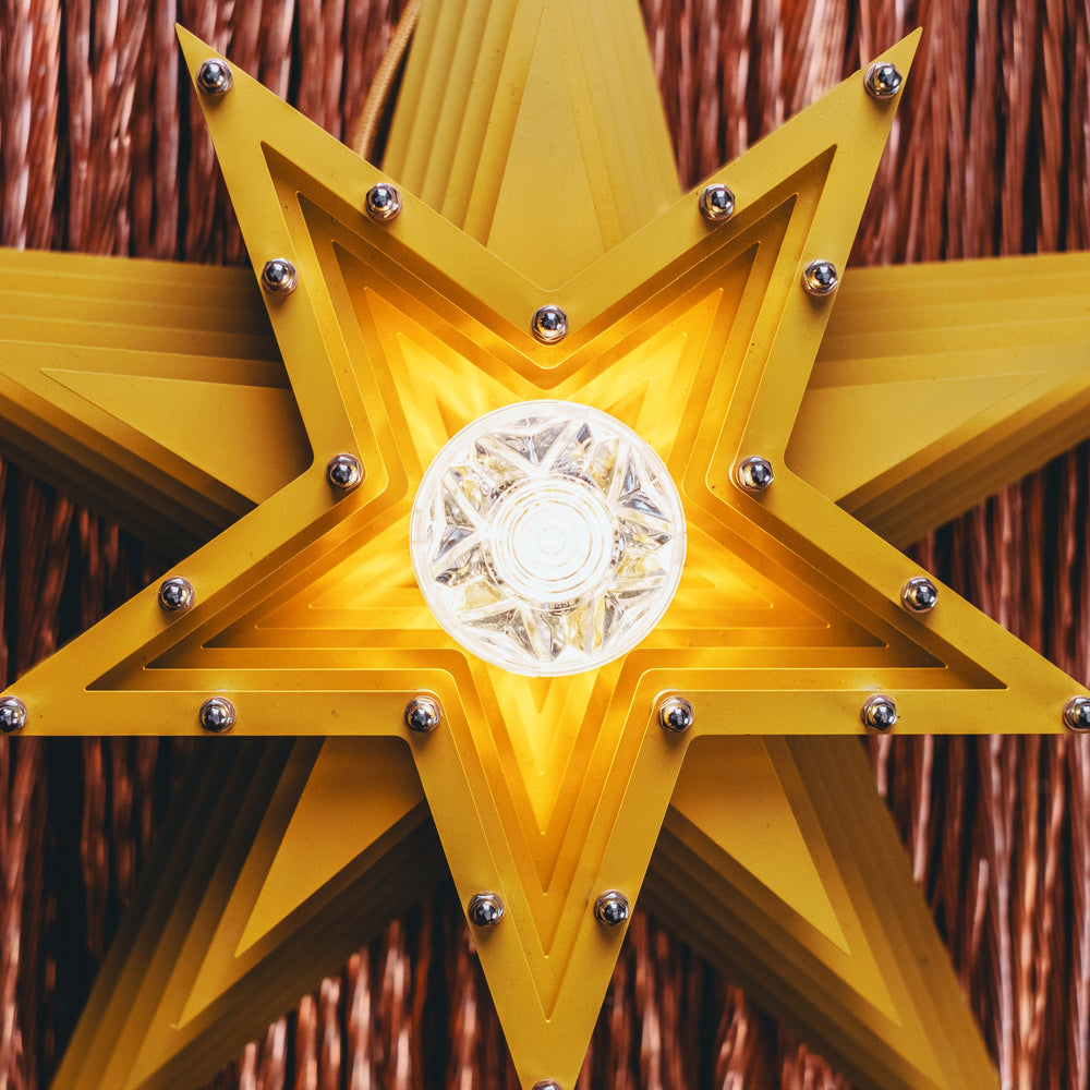 Mini Fairground Sun Star lamp handcrafted from layered steel and aluminium, finished in vibrant yellow with a central lightbulb and mounted against copper wire strands.