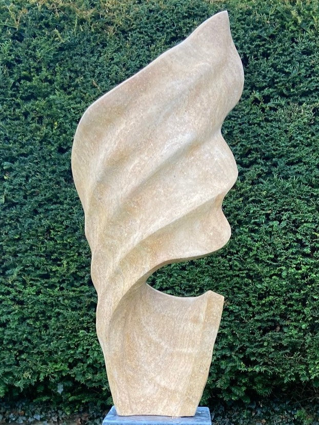 Billow 1 by Brendan Cullen, carved from Ancaster Weatherbed Limestone, a tall sandstone-toned sculpture with soft flowing ridges that rise in a twisting, wave-like form, mounted on a dark stone base.
