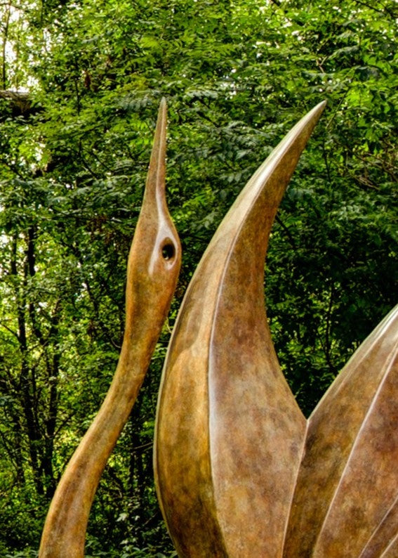 Simon Gudgeon bronze sculpture Bird of Happiness featuring an elegant crane-inspired contemporary bronze form with sweeping curved lines displayed within a landscaped garden setting.