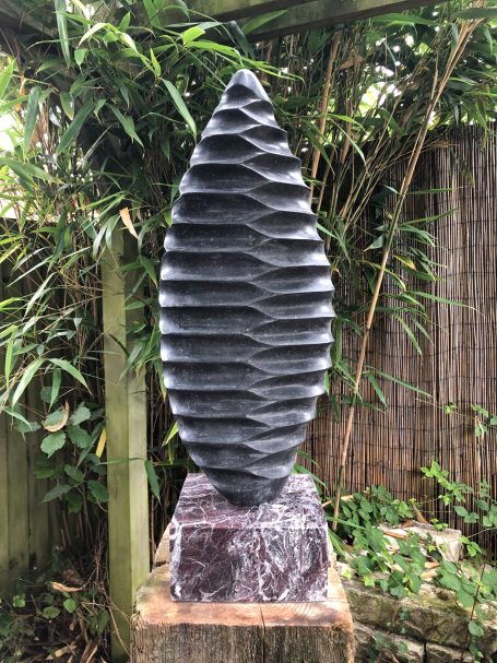 Bivalve Blade by Brendan Cullen, a tall hand-carved Kilkenny limestone sculpture with a tapered, leaf-like form and precise, rhythmic ridges reminiscent of shells or ancient fossils, mounted on a polished marble base.
