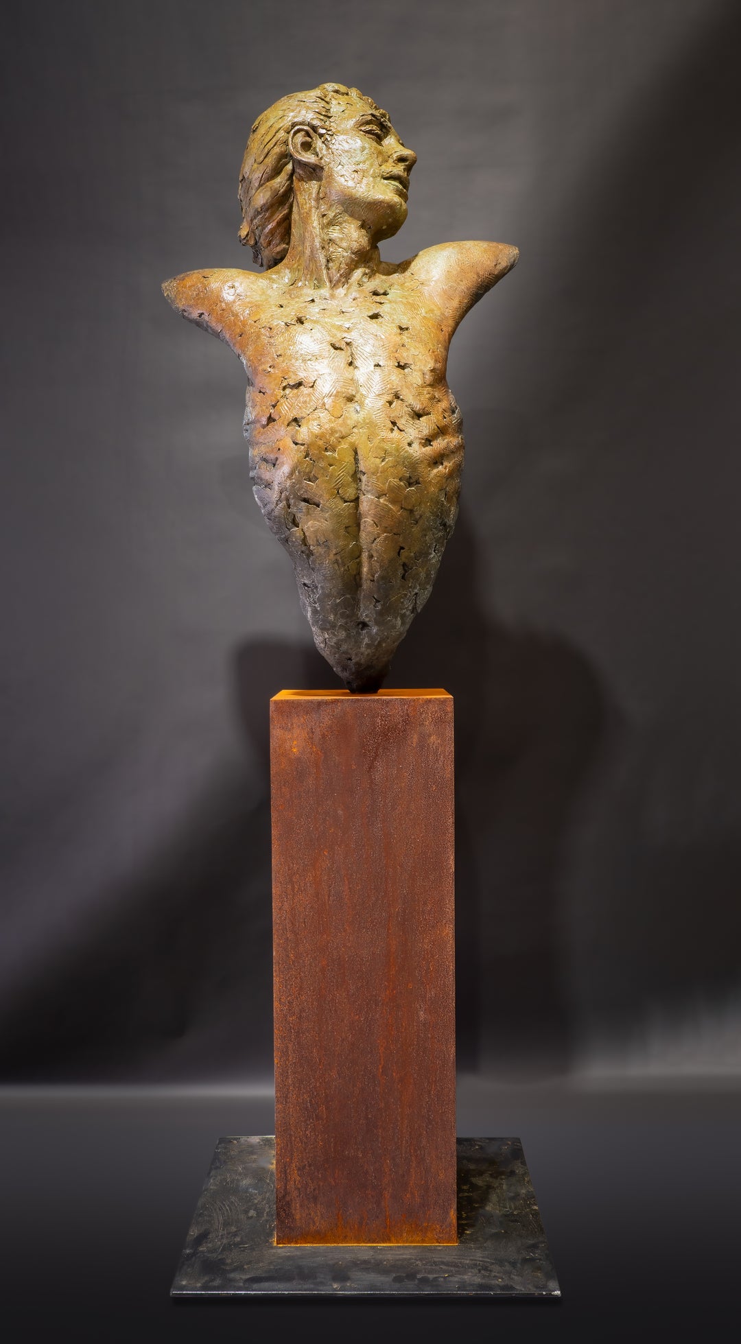 Nicola Godden Bliss Icarus bronze sculpture portraying a stylised human figure rising upward with arms extended and head turned, evoking a moment of release and quiet strength. The elongated form suggests lift and motion while remaining grounded through a solid Corten steel base. The textured bronze surface carries depth and variation, with light catching across its contours to enhance the sense of movement and presence.