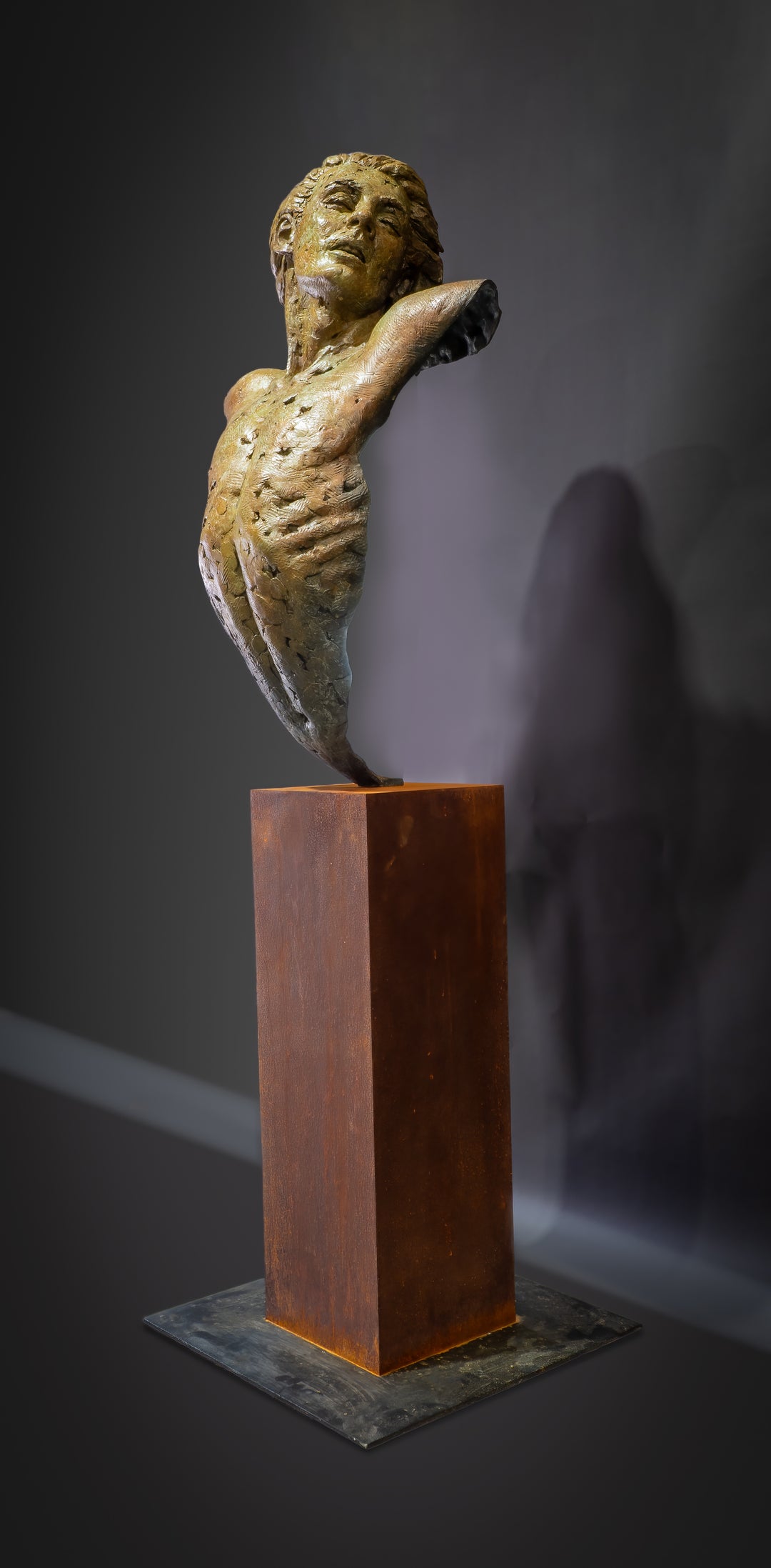 Nicola Godden Bliss Icarus bronze sculpture portraying a stylised human figure rising upward with arms extended and head turned, evoking a moment of release and quiet strength. The elongated form suggests lift and motion while remaining grounded through a solid Corten steel base. The textured bronze surface carries depth and variation, with light catching across its contours to enhance the sense of movement and presence.