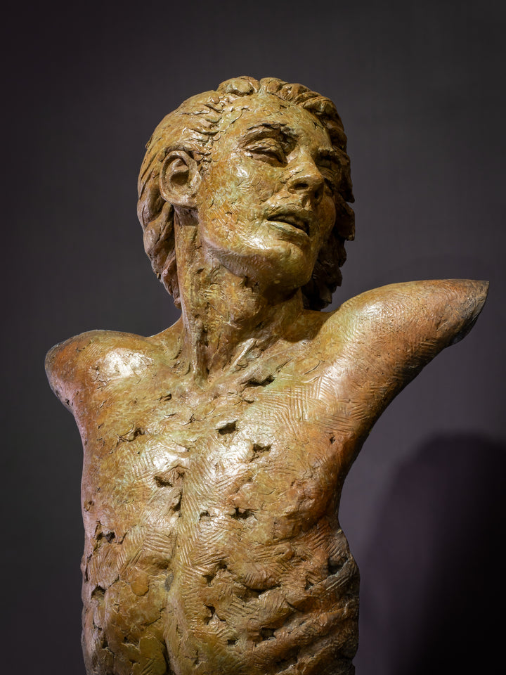 Nicola Godden Bliss Icarus bronze sculpture portraying a stylised human figure rising upward with arms extended and head turned, evoking a moment of release and quiet strength. The elongated form suggests lift and motion while remaining grounded through a solid Corten steel base. The textured bronze surface carries depth and variation, with light catching across its contours to enhance the sense of movement and presence.