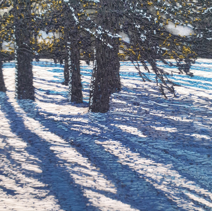 Textile artwork depicting blue winter shadows cast by trees across snow, created with freehand machine embroidery on painted silk.
