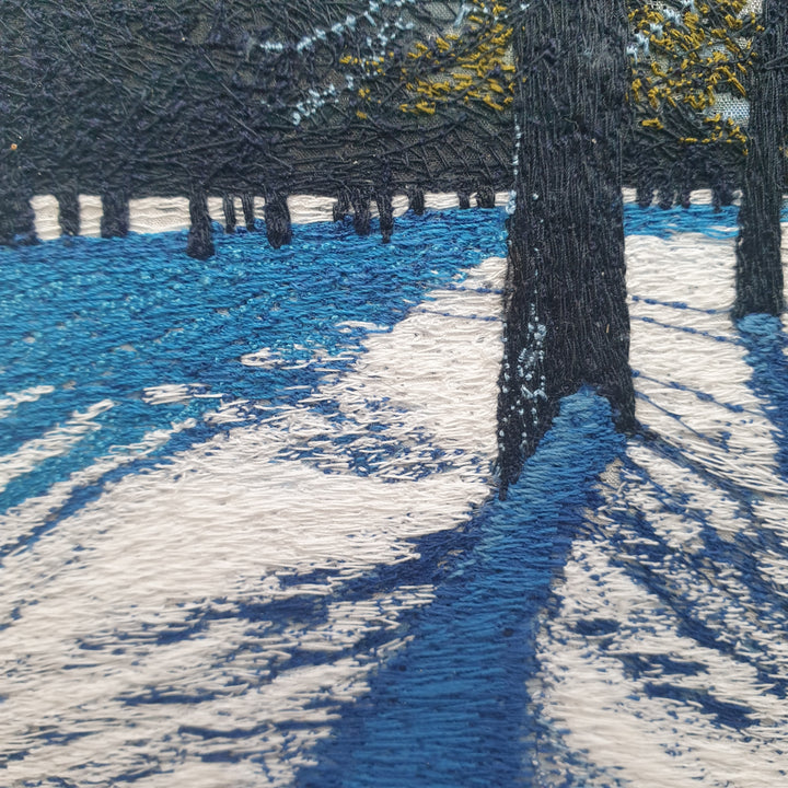 Textile artwork depicting blue winter shadows cast by trees across snow, created with freehand machine embroidery on painted silk.