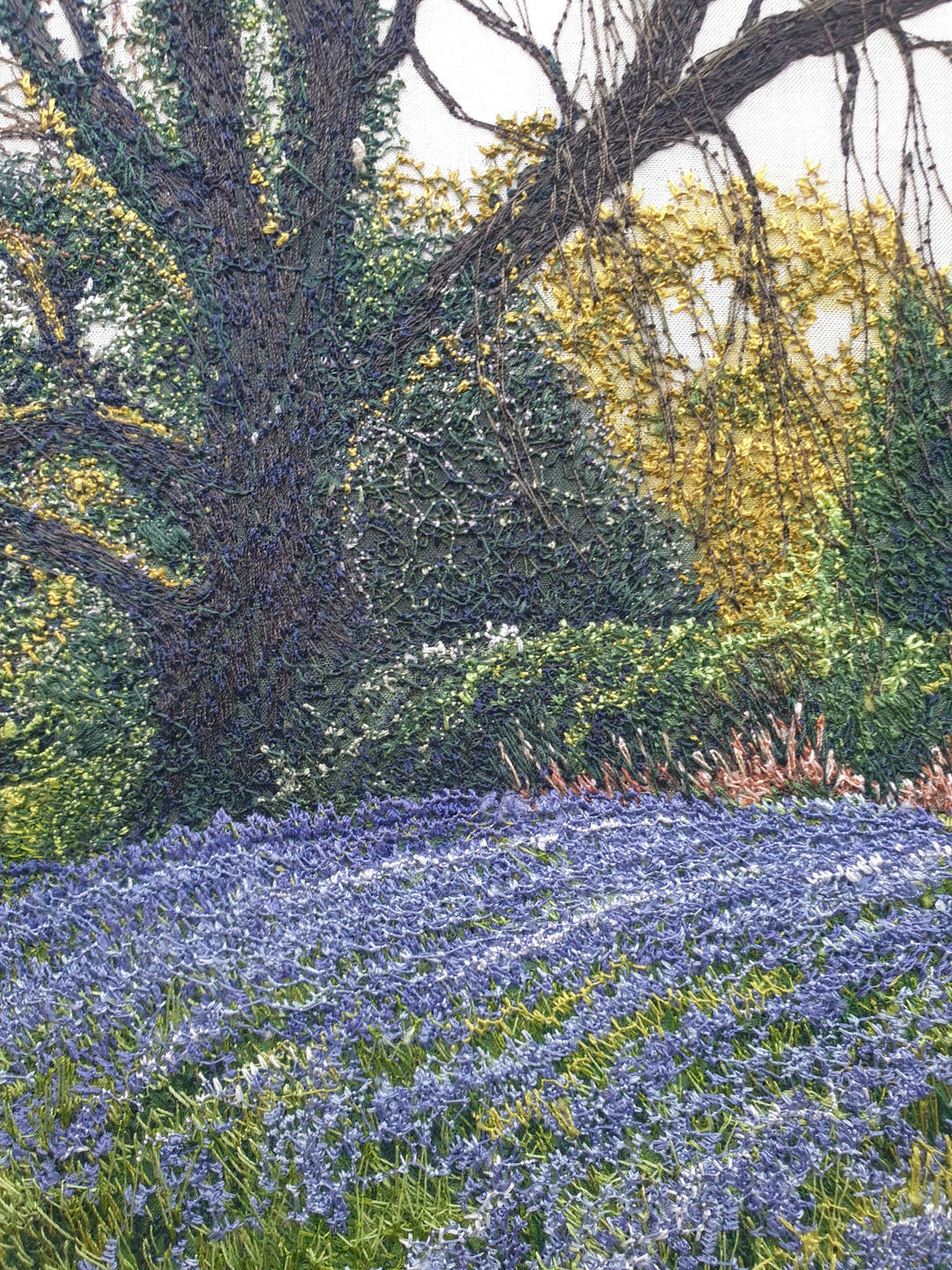 Textile artwork depicting a bluebell-covered landscape with a large oak tree and winding path, created with freehand machine embroidery on painted silk.