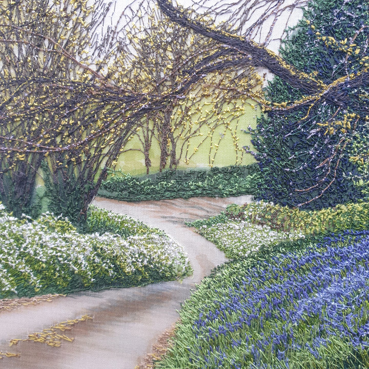 Textile artwork depicting a bluebell-covered landscape with a large oak tree and winding path, created with freehand machine embroidery on painted silk.