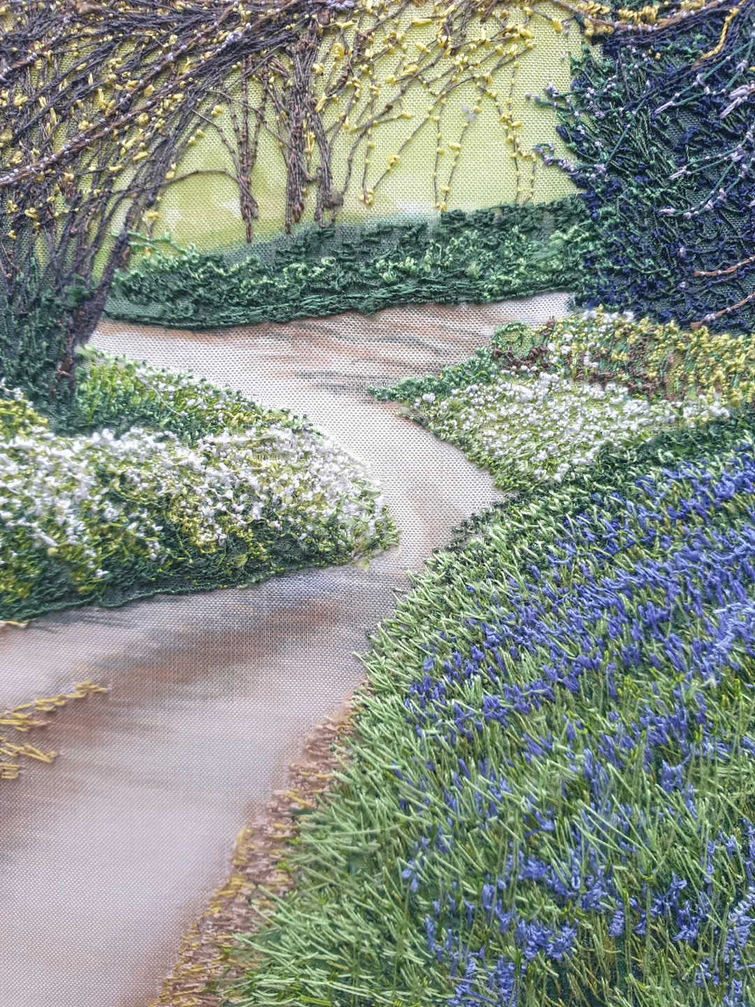 Textile artwork depicting a bluebell-covered landscape with a large oak tree and winding path, created with freehand machine embroidery on painted silk.
