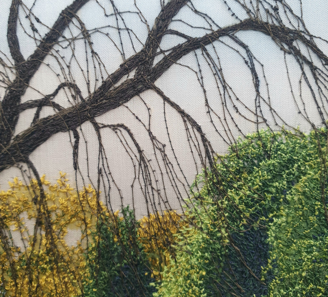 Textile artwork depicting a bluebell-covered landscape with a large oak tree and winding path, created with freehand machine embroidery on painted silk.